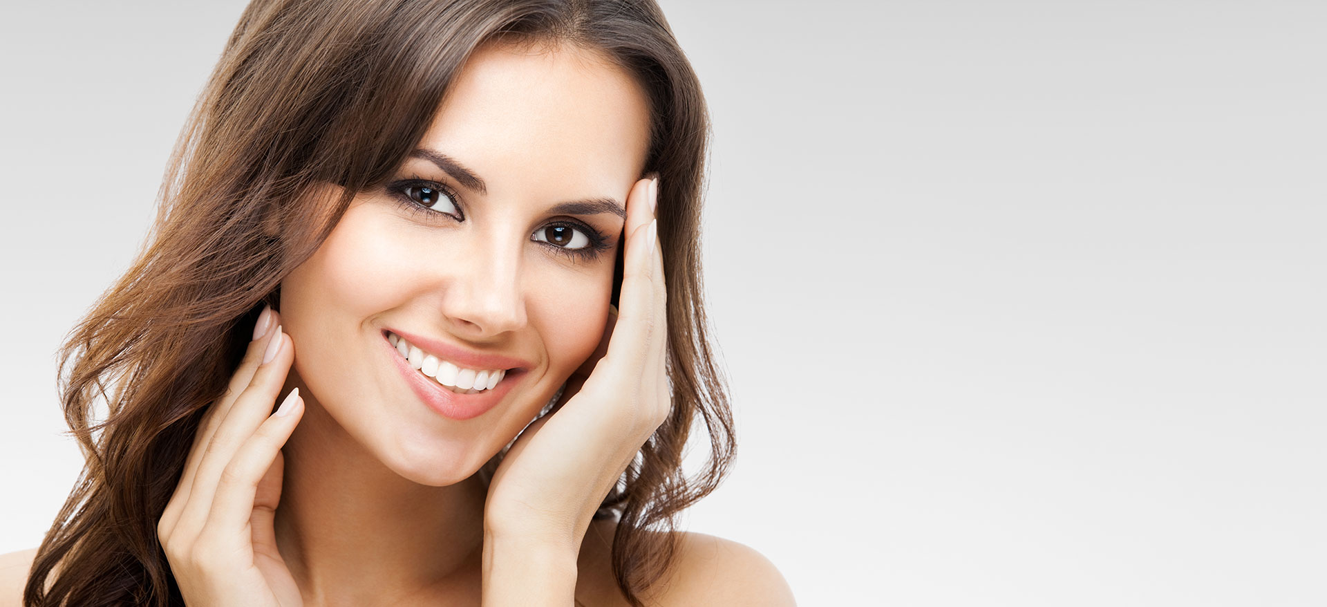 A woman with her eyes closed, smiling at the camera, while looking directly into it.