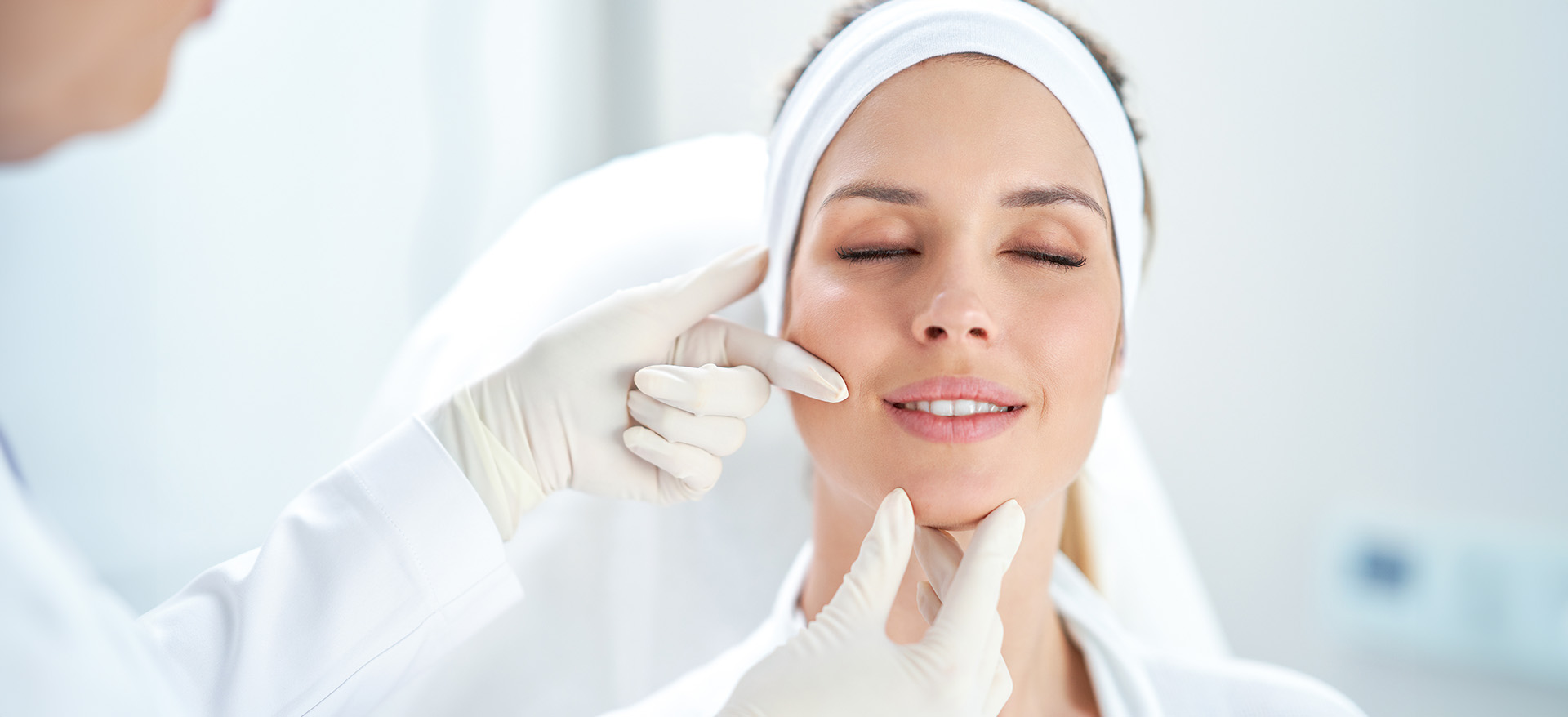 A woman receiving a facial treatment at a beauty salon with a therapist applying a creamy substance to her face while seated in a chair.