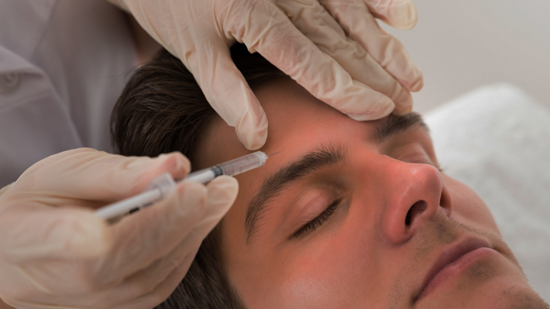 A man receiving cosmetic treatment with medical professionals attending to his face.