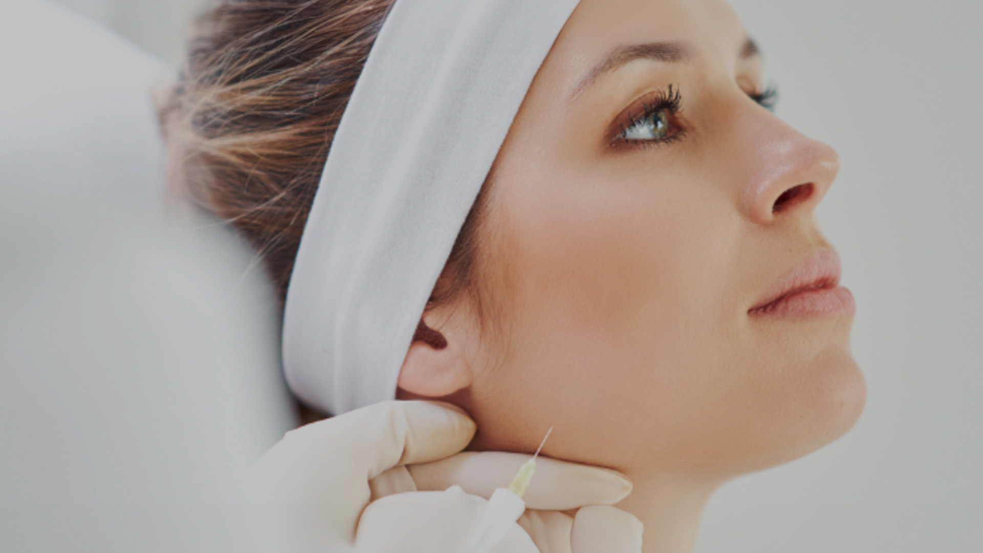 The image shows a person receiving a facial treatment with a medical device, possibly at a spa or beauty clinic, as indicated by the presence of a headband and the professional setting.