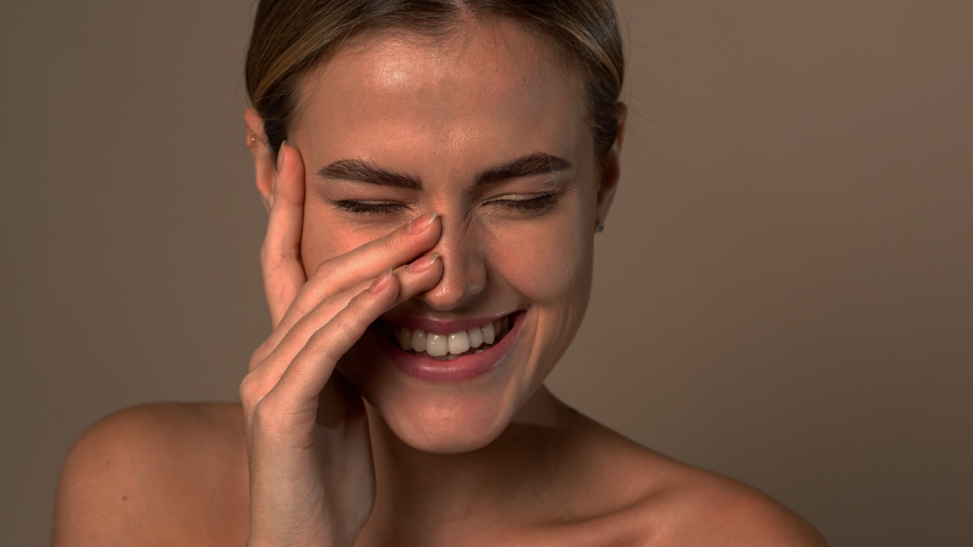 A woman with her eyes closed, holding her nose, smiling subtly.