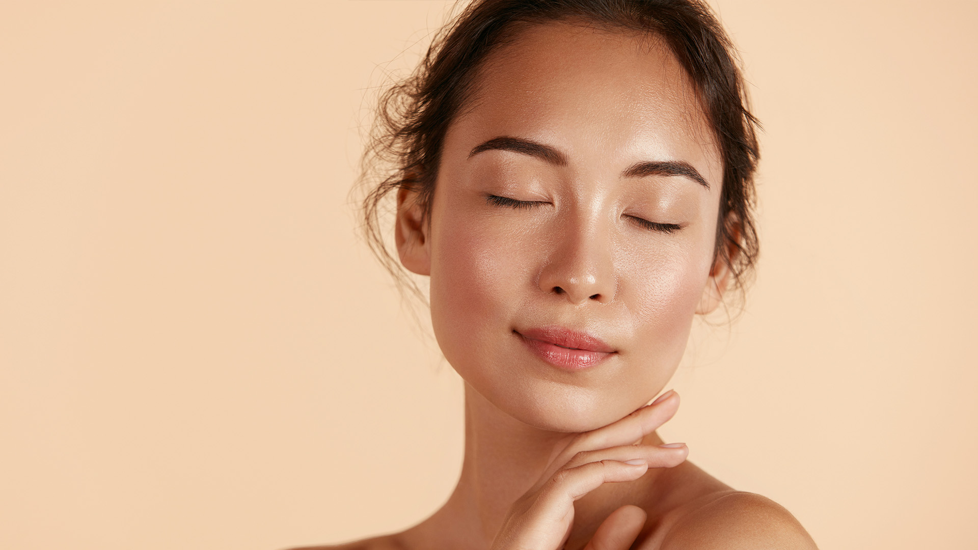 A woman with her eyes closed, looking upwards, against a soft, warm background.