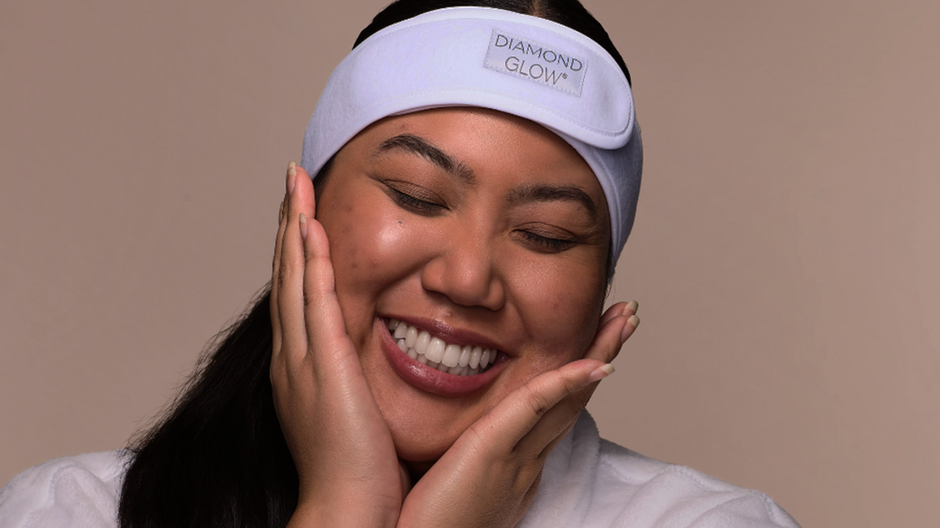 A woman with a radiant smile wearing a white visor and holding her face with both hands.