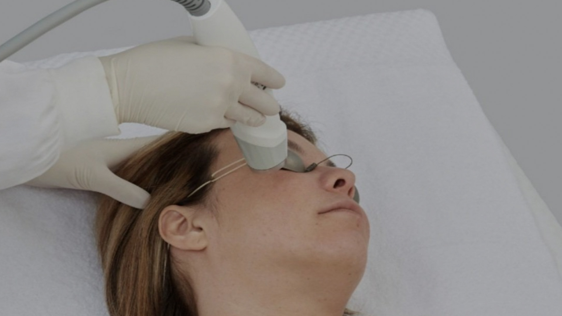 Woman receiving laser hair removal treatment with a device held by a hand wearing protective gloves.