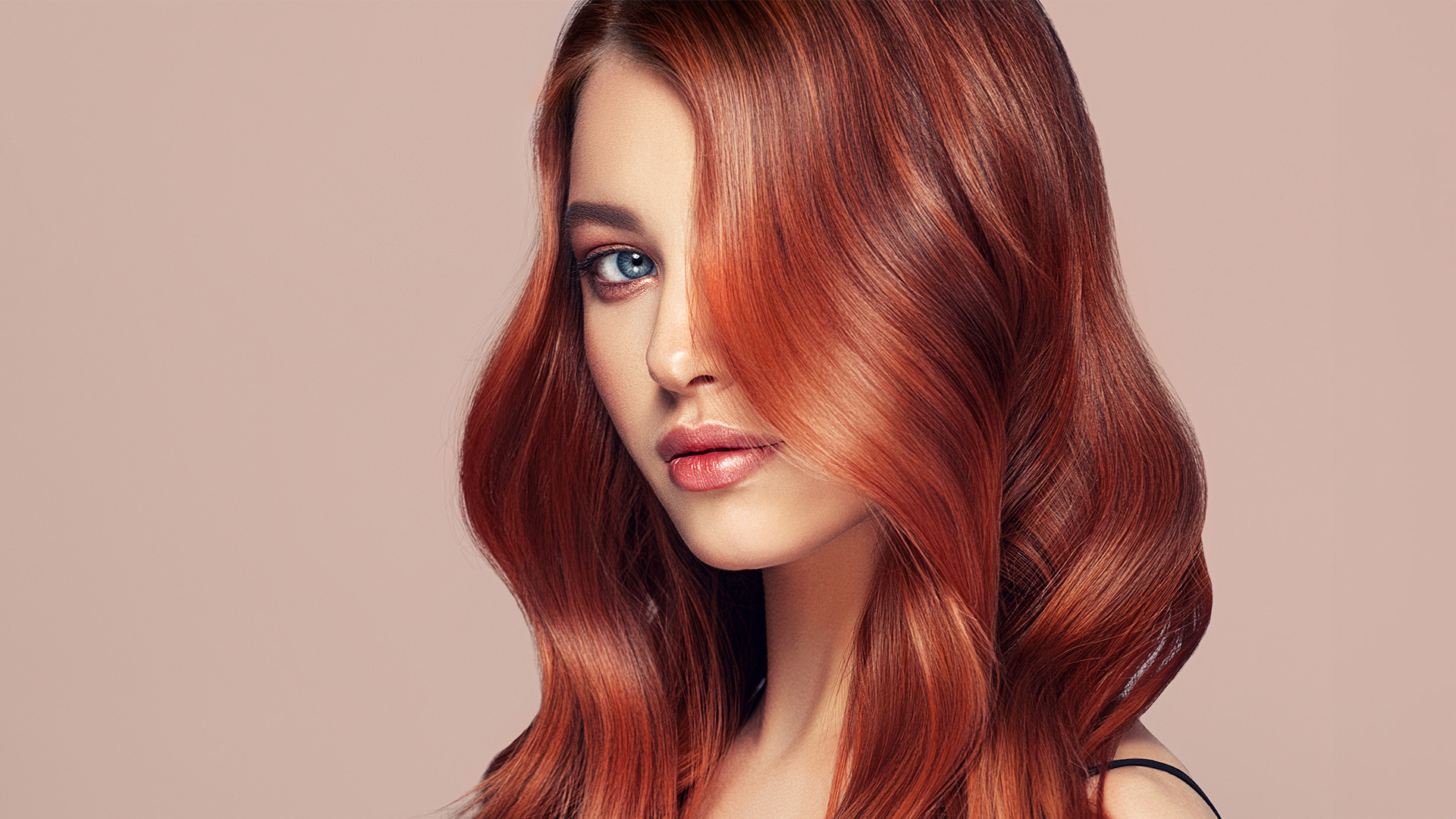 A woman with red hair gazes directly at the camera against a neutral background.