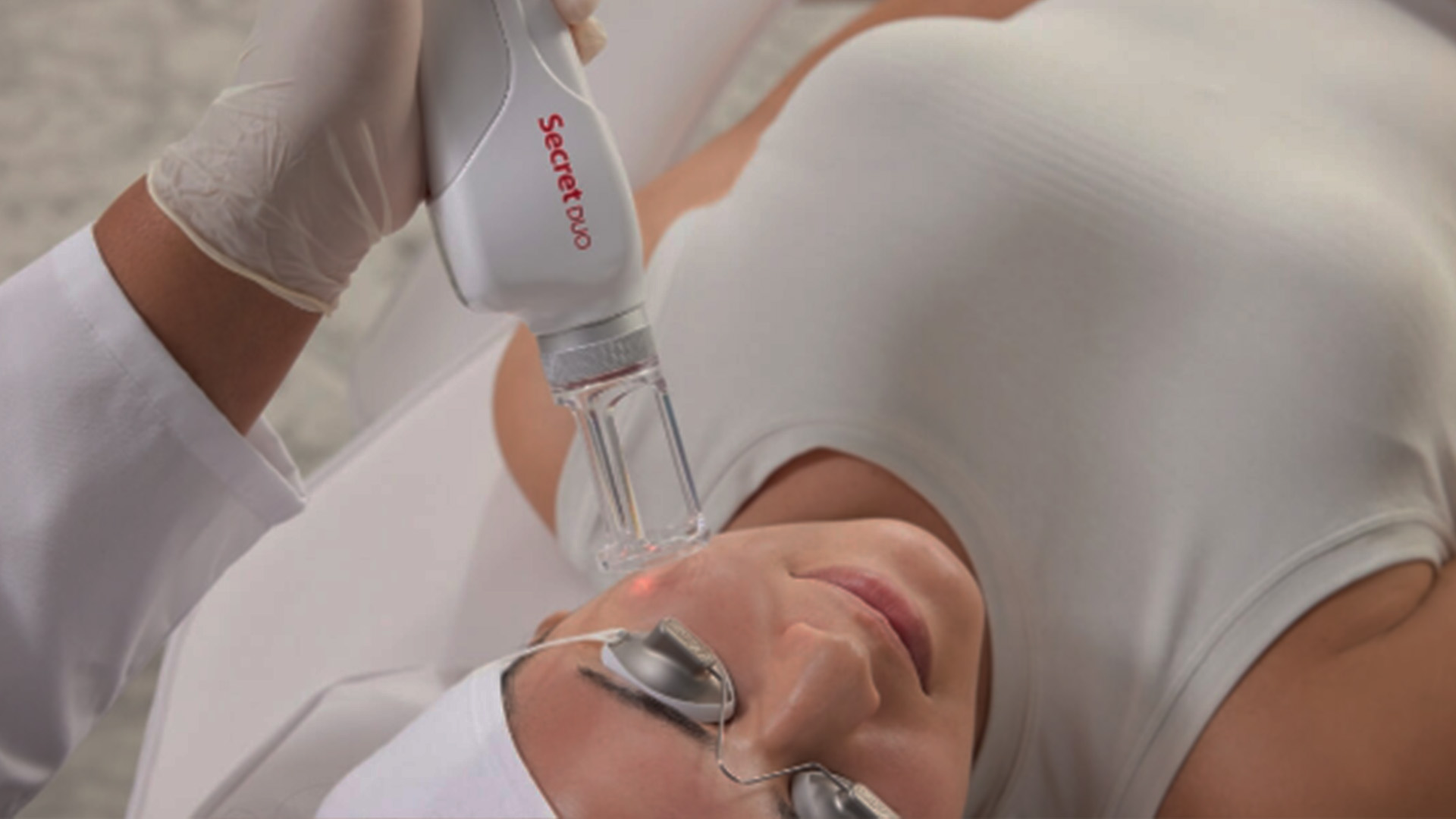 A person receiving a facial treatment with a device being applied by another individual wearing medical gloves.