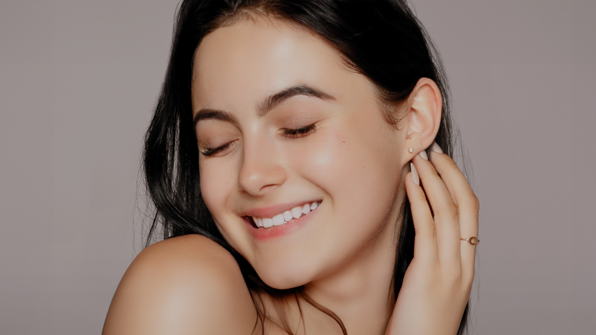 A woman with closed eyes and a smile, looking upwards, against a neutral background.