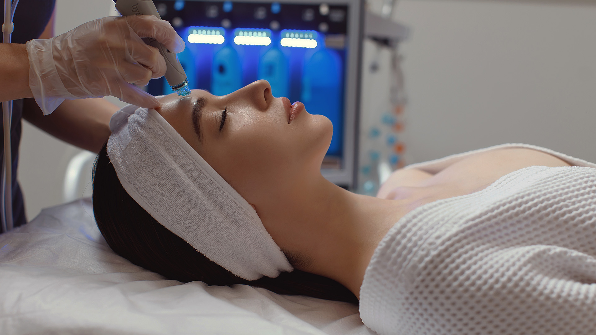 The image shows a person receiving a facial treatment with a device being applied to their face by a professional.