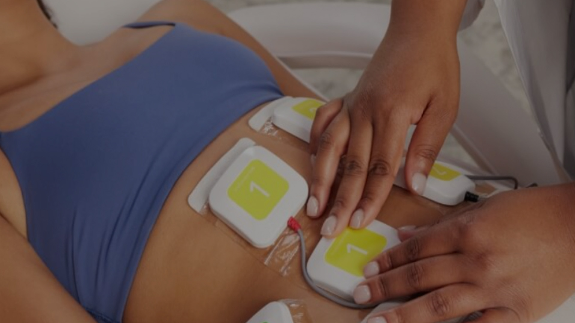 An image of a person receiving an ECG test with various electrode pads attached to their body while a technician monitors the readings on a device.