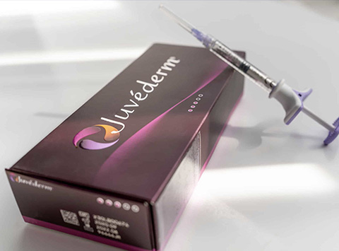 The image shows a boxed product with a brand name  Juvaderm  on a white surface, accompanied by a syringe with a purple plunger.