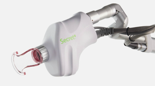 The image shows a robotic arm with a mechanical grip holding a small pink object, which appears to be a medical device, possibly an endoscope, against a white background.