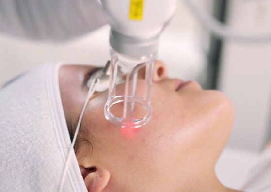 The image depicts a person receiving a medical treatment involving a device that appears to be a laser or light therapy machine, with a red beam focused on their face.